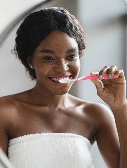 Woman with braces smiling while brushing her teeth