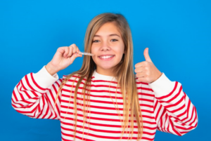 Young girl on blue background smiling and holding Invisalign tray